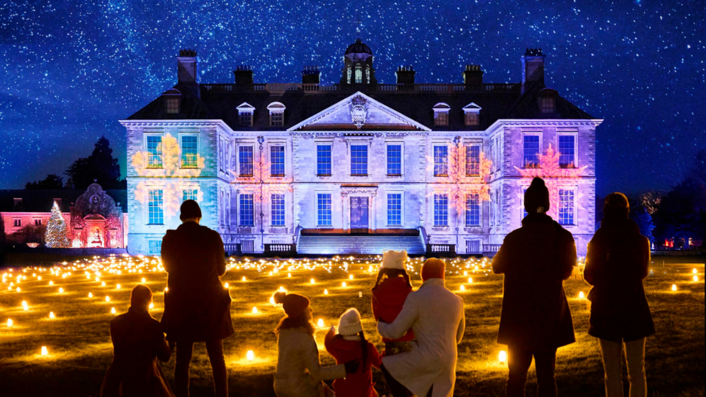 Christmas at Belton - a family looking at Belton House lit up in purple with festive lights on the grounds in front. Christmas at Belton - a family looking at Belton House lit up in purple with festive lights on the grounds in front.