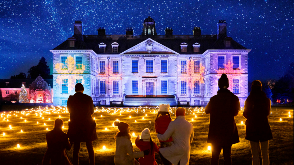 Christmas at Belton - a family looking at Belton House lit up in purple with festive lights on the grounds in front.