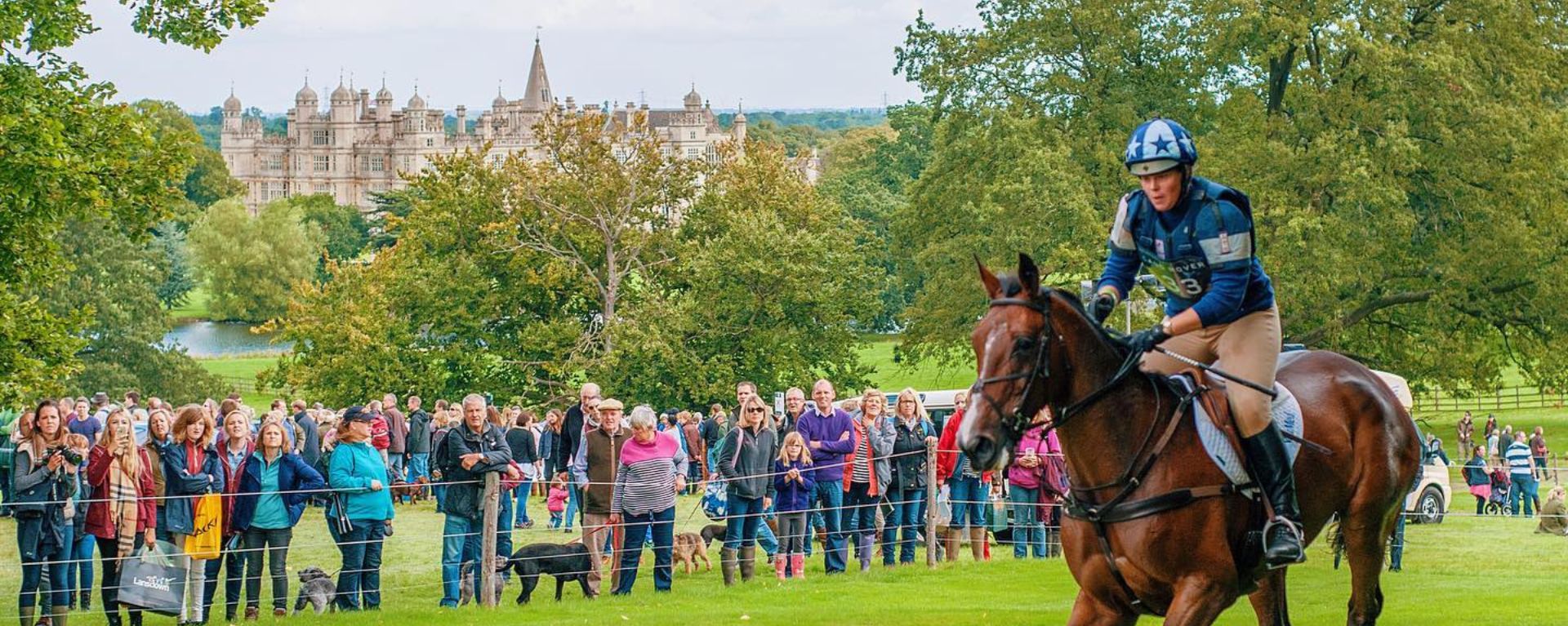 Crowd of spectators watching a horse rider at the Burghley Horse Trials, with a view of Burghley House in the distance. Crowd of spectators watching a horse rider at the Burghley Horse Trials, with a view of Burghley House in the distance.