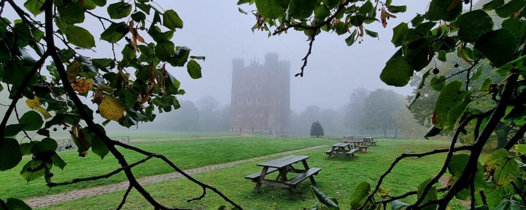 A misty view of Tattershall Castle through the leaves